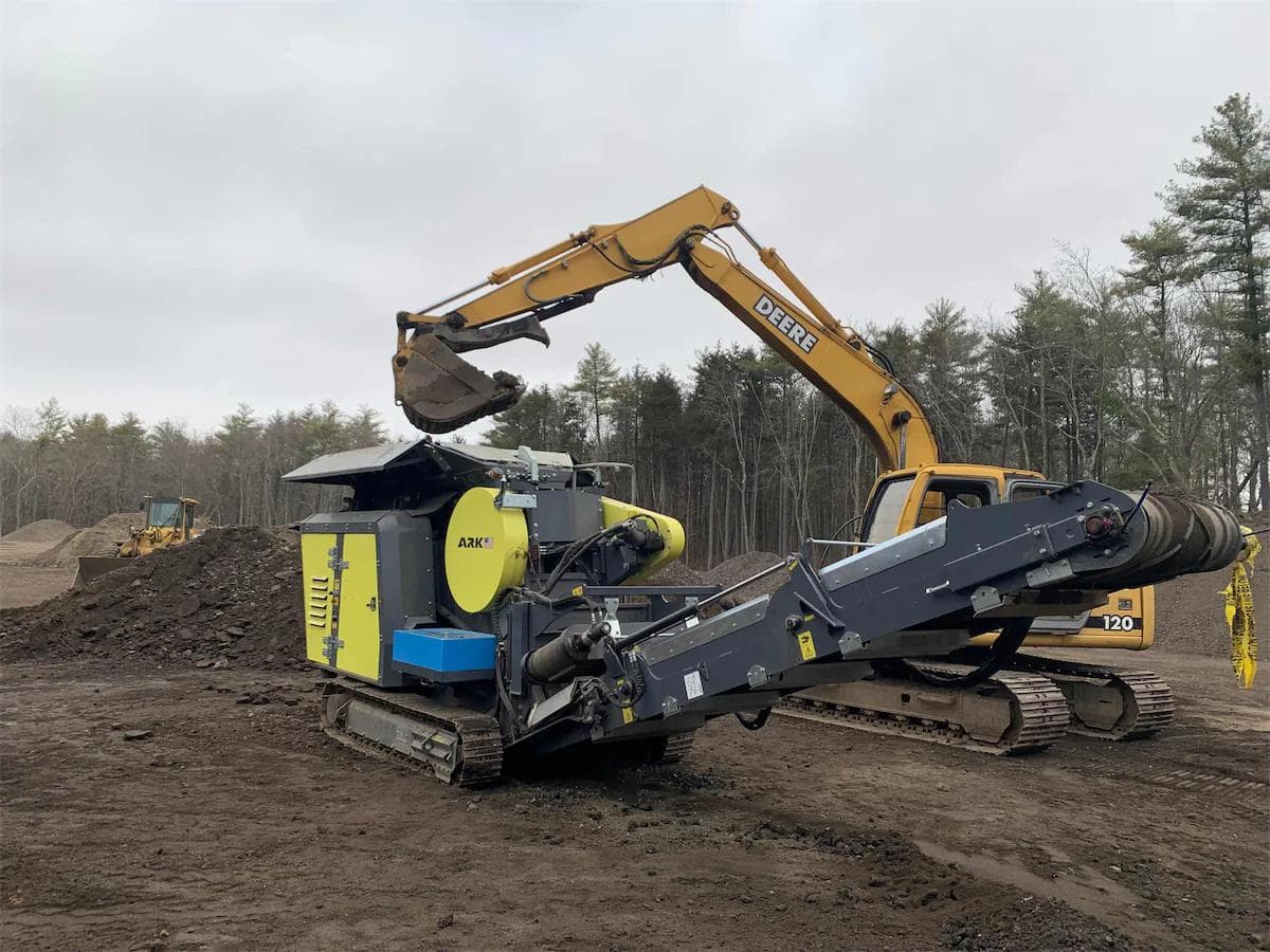 yellow john deere excavator feeding ashalt into a yellow and gray ARK 704 jaw crushing machine
