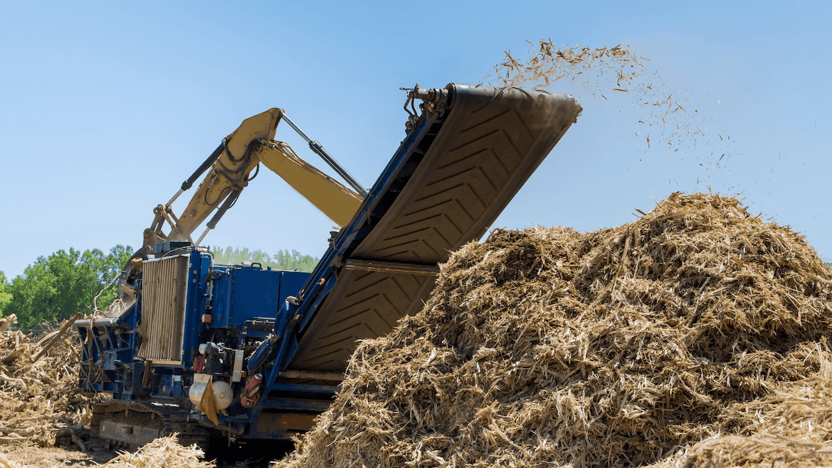 blue horizontal grinder shredding wood waste into a large pile