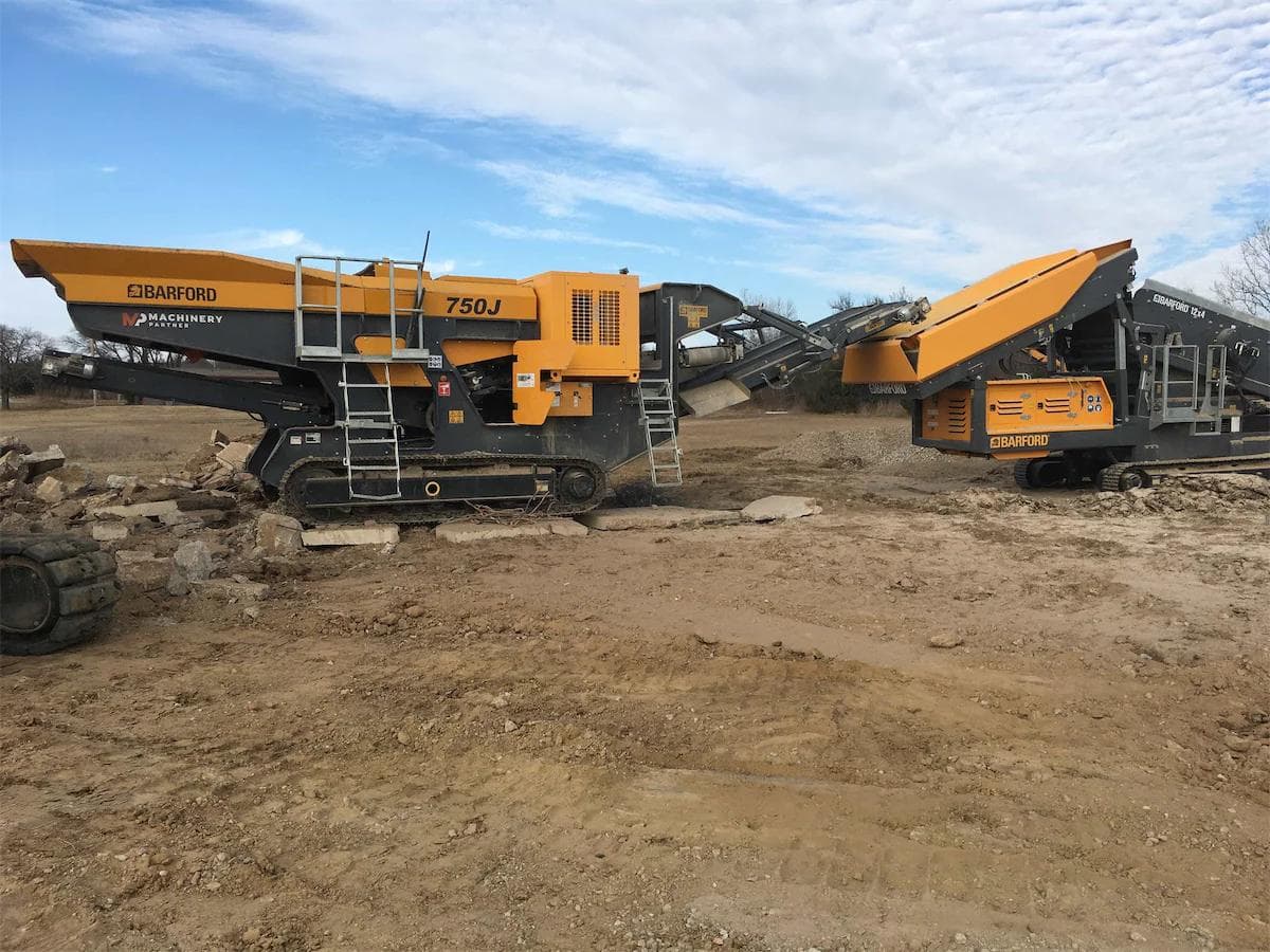 yellow barford 750j jaw crusher feeding material into a barford sr124 3-way scalping screener on a dusty construction site