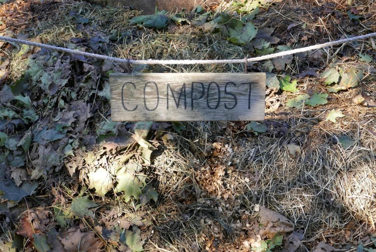 a compost pile at a local farm that is made up of leaves, grass and other compostable material. The pile has a wooden compost sign over it held up with rope