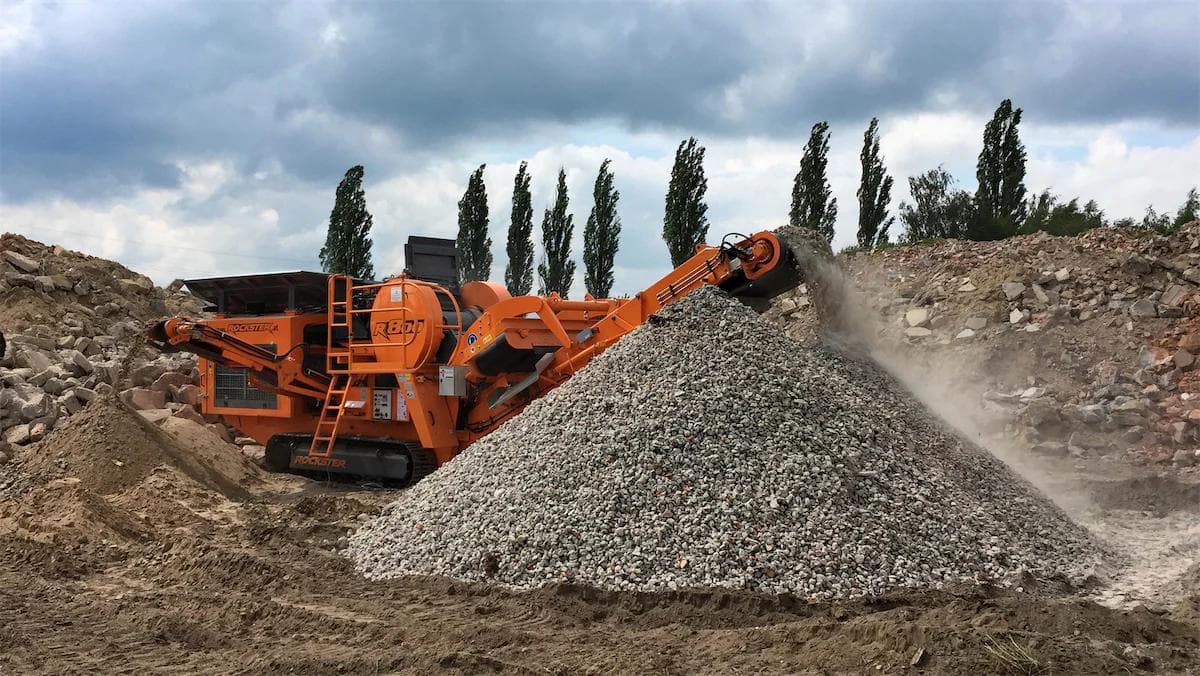 orange Rockster R800 impact crusher crushing a large pile of concrete into a stockpile onsite
