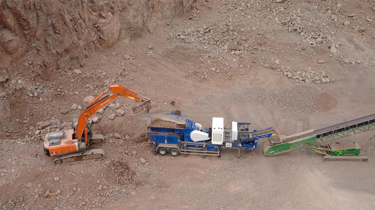 Omega j1065t being fed by an excavator, crushing material and feeding a conveyor on a quarry