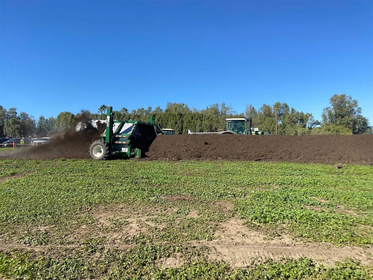 green windrow turner aerating a pile of compost