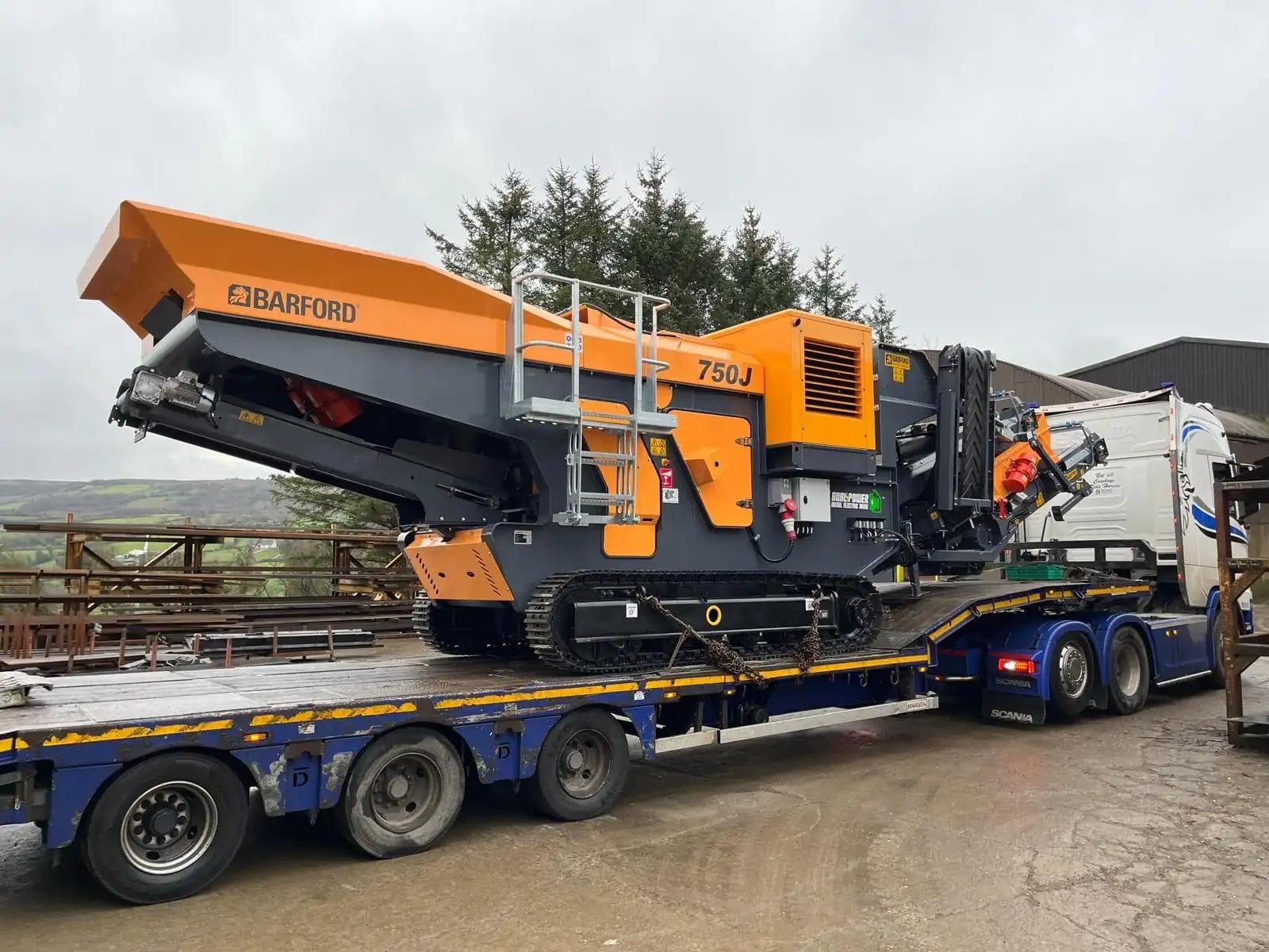 Barford 750J RS being transported on a gooseneck trailer and truck